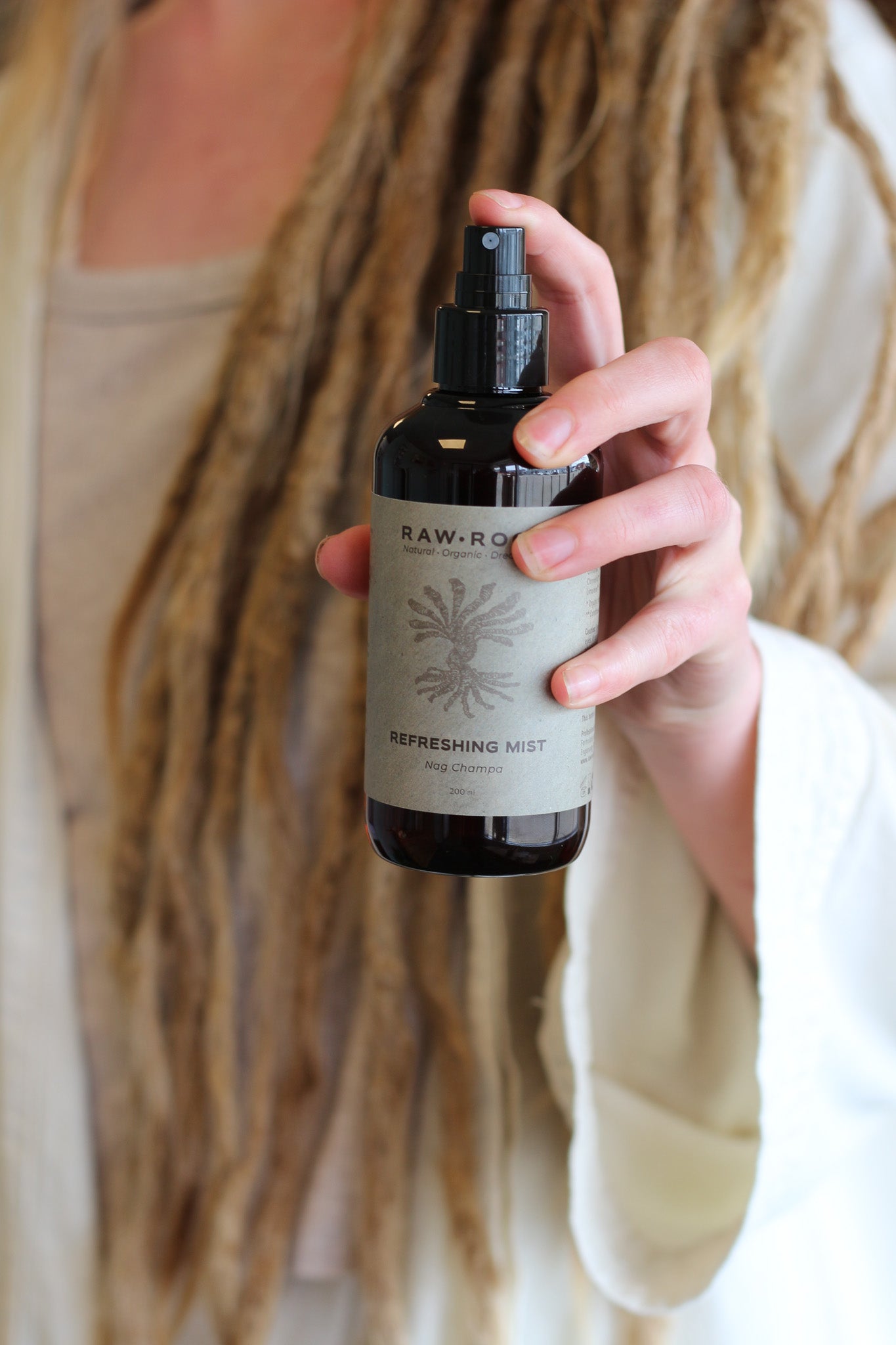 Person holding a bottle of 'Raw-Roots' refreshing mist with visible dreads.